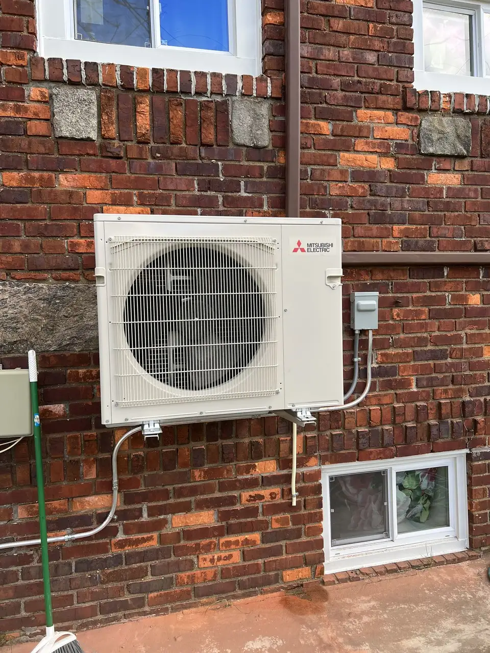 Mitsubishi ductless condenser on a brick wall in Queens, installed by Electric A/C Inc